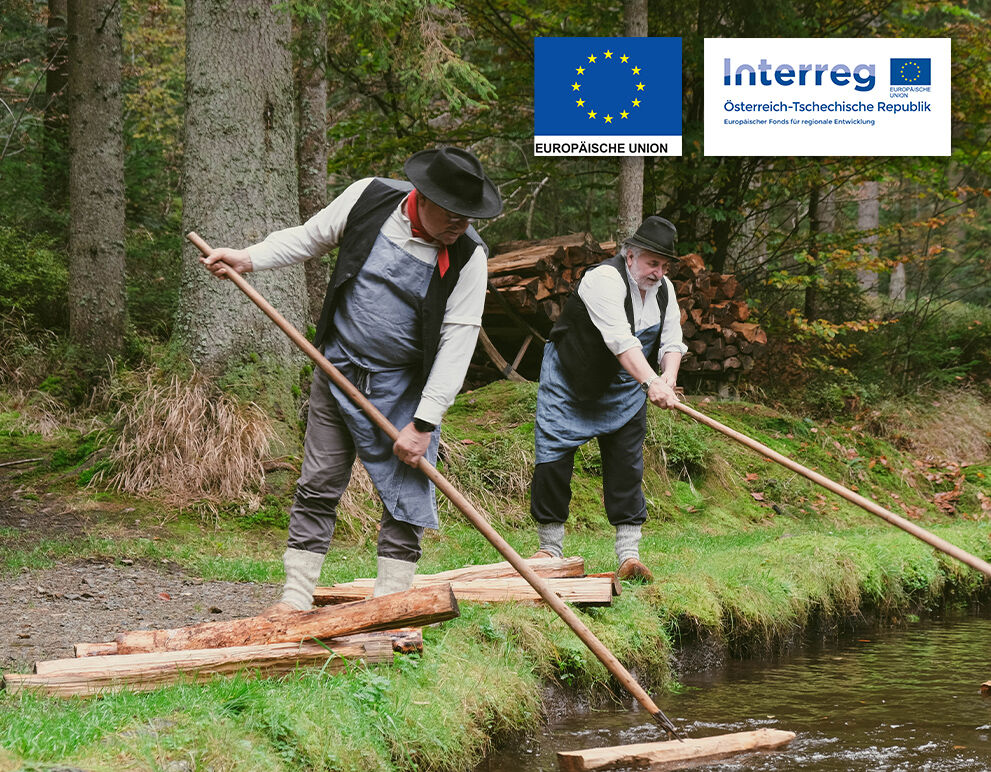 Zwei Holzschwemmer in traditioneller Kleidung floessen Holzscheiter in einem Wassekanal.