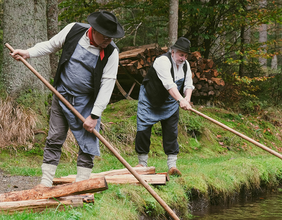 Zwei Arbeiter ziehen in traditioneller Arbeitskleidung Holz aus dem Schwemmkanal