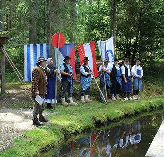 Schwemmdirektor steht vor dem Wasserkanal und hält eine Ansprache. Im Hintergrund sieht man die Schwemmergruppe in ihrer Arbeitskleidung. (Vergrößerte Ansicht)